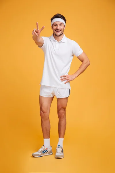 Happy handsome young male athlete standing and showing victory sign — Stock Photo, Image