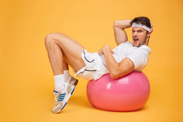 Deportista haciendo abdominales en la pelota de fitness sobre fondo naranja — Foto de Stock