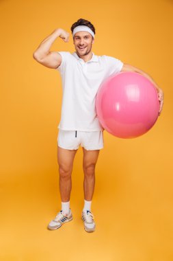 Young handsome sportsman holding fitness ball and showing biceps