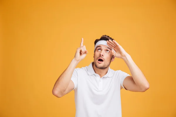 Sorprendido joven deportista atractivo mirando y señalando hacia arriba — Foto de Stock