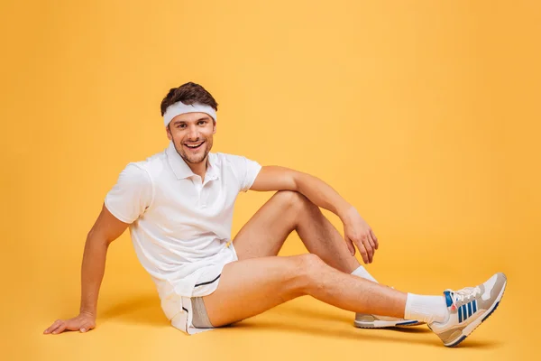Full längd av glada attraktiva unga Sportsman sittande och leende — Stockfoto