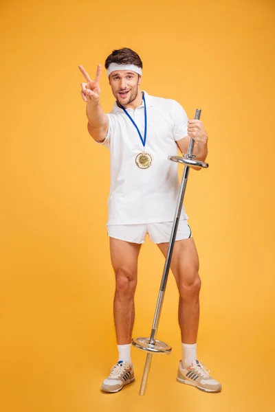 Happy young sportsman with barbell standing and showing victory sign — Stock Photo, Image