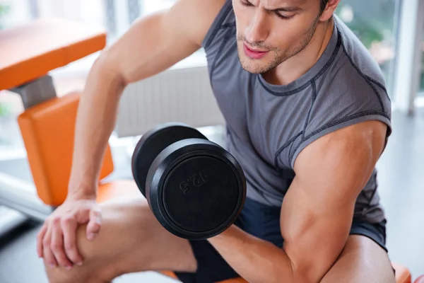 Hombre atleta sentado y haciendo ejercicio con mancuerna en el gimnasio —  Fotos de Stock