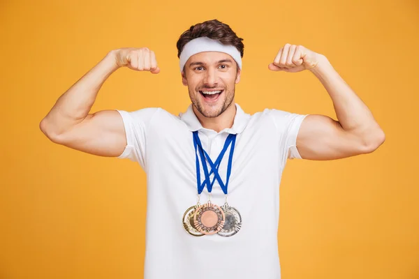Cheerful young spotrsman with three medals showing biceps — Stock Photo, Image