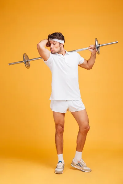 Amusing young sortsman with barbell showing and kissing his biceps — Stock Photo, Image