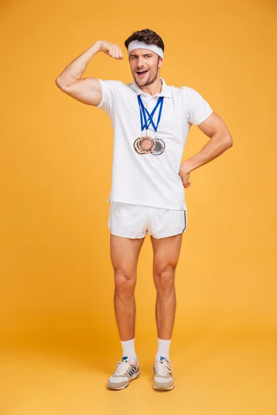 Magabiztos férfi sportoló három érmet, állandó, és bemutatja a bicepsz — Stock Fotó