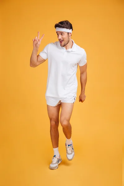 Cheerful young sportsman running amd showing peace sign — Stock Photo, Image