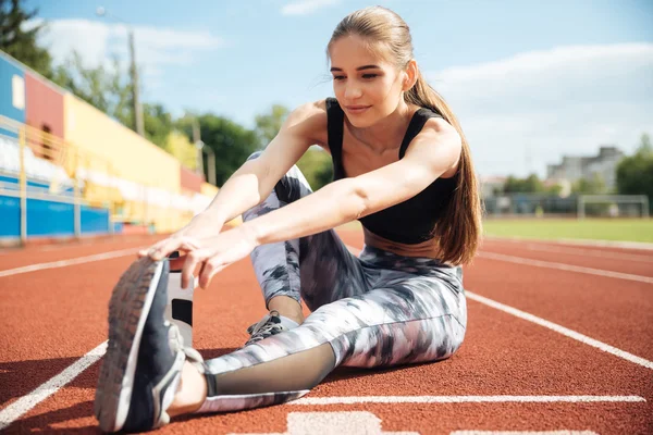 Sportowiec kobieta siedzi i rozciąganie nogi na stadion — Zdjęcie stockowe