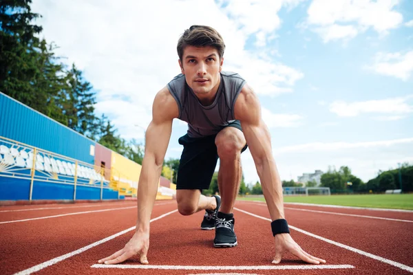 Jovem em posição inicial para correr em pista desportiva — Fotografia de Stock