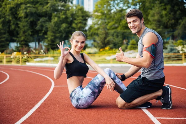 Young beautiful happy couple doing sports exercises at the stadium — Stock Photo, Image