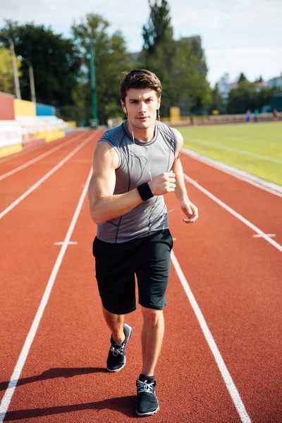 Hombre de deportes concentrado corriendo por la pista del estadio con auriculares — Foto de Stock