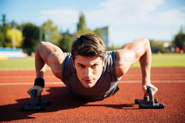 Young male athlete makes push ups on a racetrack