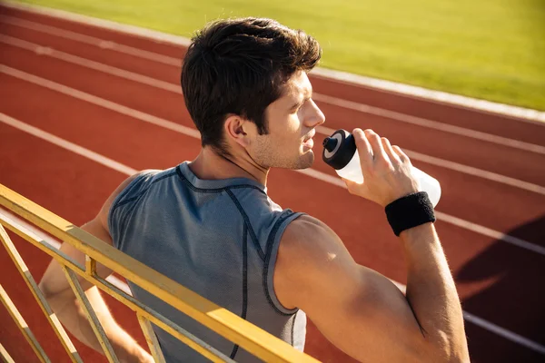 Junger Sportler trinkt Wasser, während er sich an das Geländer lehnt — Stockfoto