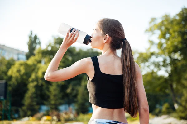 Női sportoló iszik víz üveg, edzés után stadionban — Stock Fotó