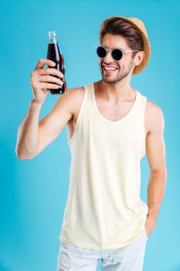 Şapka ve güneş gözlüğü soda şişe tutan gülümseyen adam