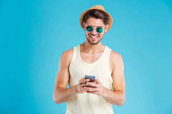 Joven feliz con sombrero y gafas de sol usando smartphone — Foto de Stock