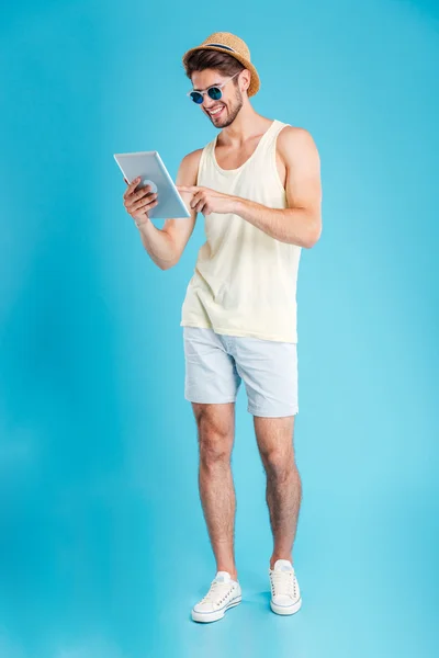 Longitud completa del joven sonriente de pie y usando la tableta — Foto de Stock