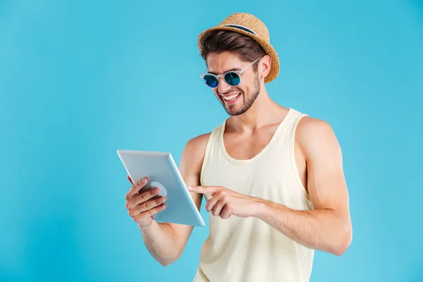 Joven alegre con sombrero y gafas de sol usando tableta — Foto de Stock