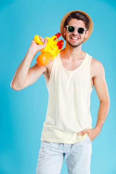 Jovem atraente feliz de pé e segurando arma de água — Fotografia de Stock