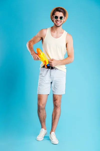 Joven joven guapo alegre de pie y posando con pistola de agua — Foto de Stock
