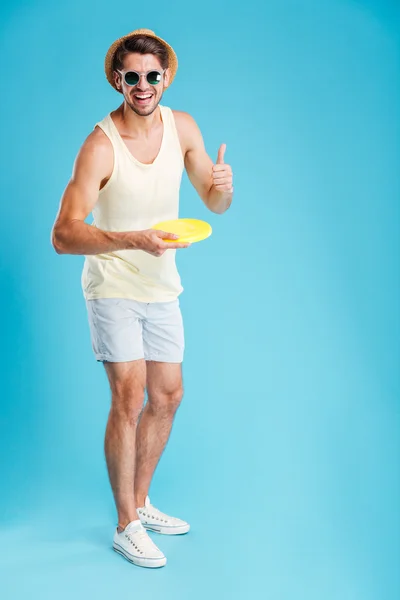 Joven alegre lanzando disco de frisbee y mostrando los pulgares hacia arriba — Foto de Stock