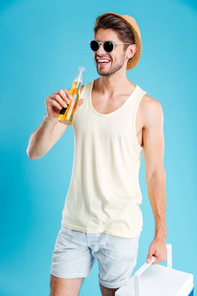Веселый молодой человек держит сумку круче и пьет пиво — стоковое фото