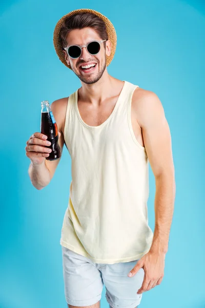 Cheerful young man in hat and sunglasses drinking soda — Stock Photo, Image