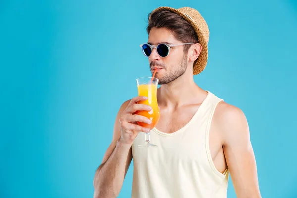 Bonito homem de chapéu e óculos de sol bebendo suco de laranja fresco — Fotografia de Stock