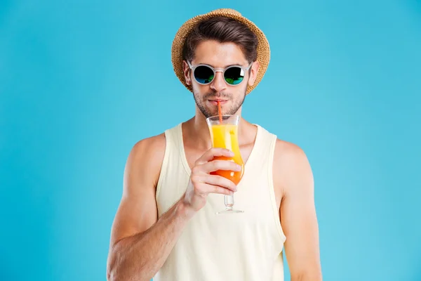 Attraktiver junger Mann mit Hut und Sonnenbrille trinkt Orangensaft — Stockfoto