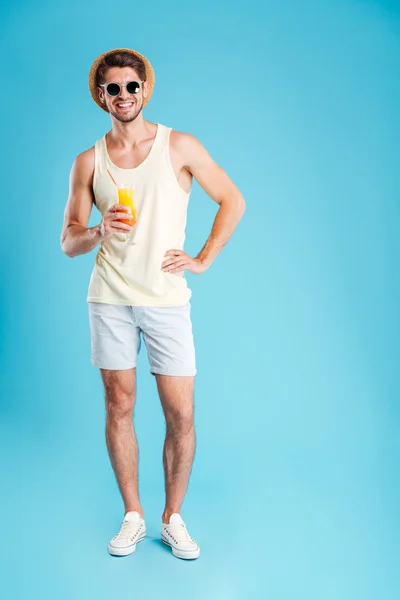 Cheerful young man standing and holding glass of orange juice — Stock Photo, Image