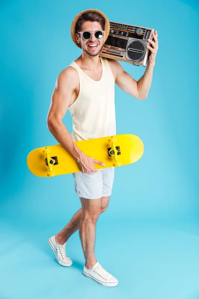 Sorrindo homem com skate amarelo andando e segurando velho boombox — Fotografia de Stock