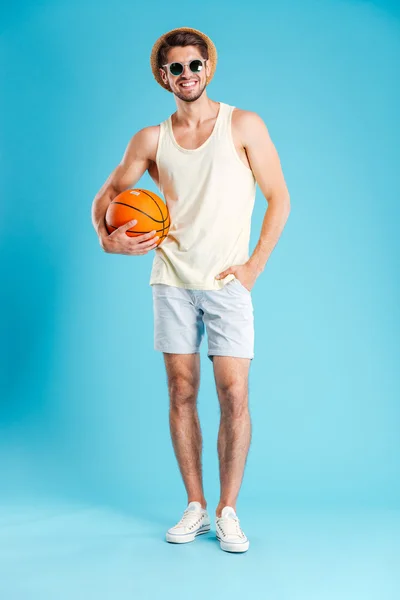 Comprimento total de homem sorrindo de pé e segurando bola de basquete — Fotografia de Stock