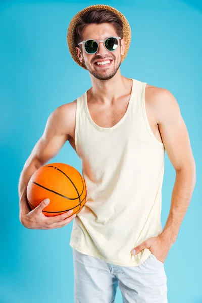 Joyeux jeune homme en chapeau et lunettes de soleil tenant ballon de basket — Photo