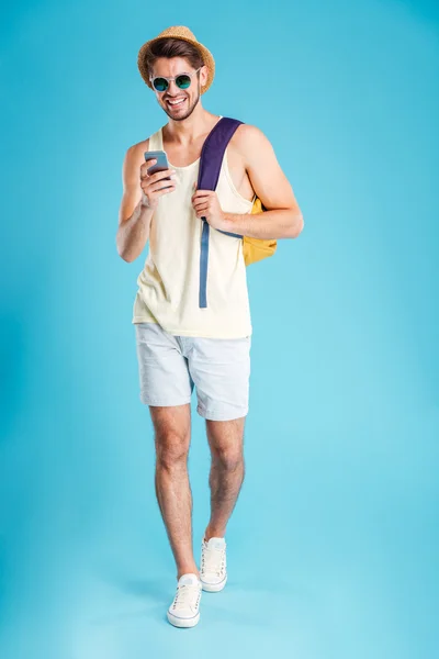 Lächelnder junger Mann mit Rucksack zu Fuß und Smartphone — Stockfoto