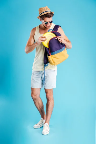 Feliz joven de pie y tomando disco de frisbee de la mochila —  Fotos de Stock