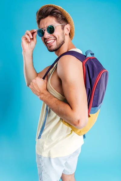 Lächelnder junger Mann mit Hut und Sonnenbrille mit Rucksack — Stockfoto