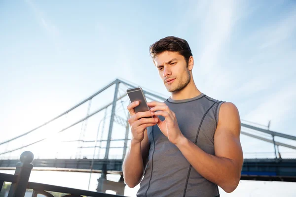 Runner utiliza el teléfono inteligente móvil y de pie en el puente — Foto de Stock