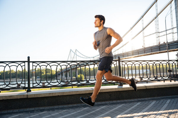 Side view of sportsman running along bridge at sunset light
