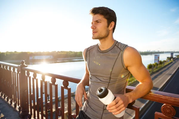 Sports man resting after running while leaning against bridge railing — Stock Photo, Image