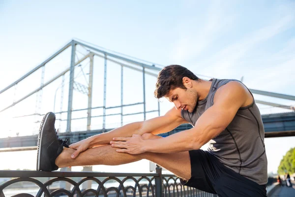 Uomo dello sport che fa stretching appoggiato alla ringhiera del ponte — Foto Stock