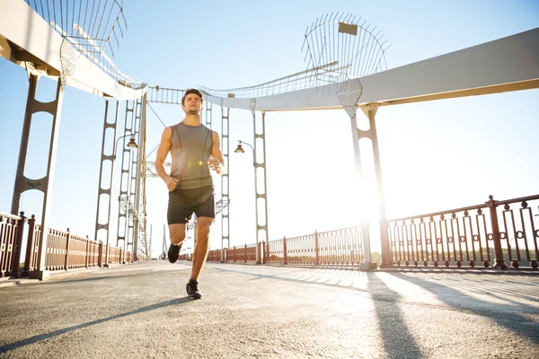 Hombre deportivo corriendo a lo largo de gran puente moderno en la luz del atardecer — Foto de Stock