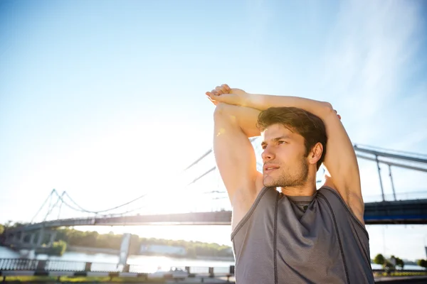 Sports man stretching at the bridge railing and looking away — Stock Photo, Image