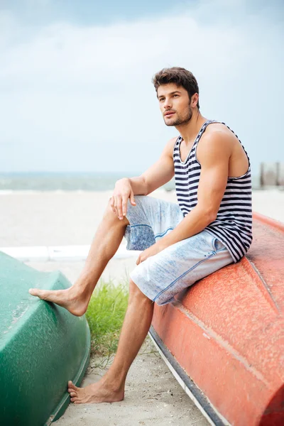 Handsome young man sitting on a fishing boat by sea — Stock Photo, Image