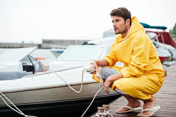 Sailor in yellow cloak holding rope at the pier — Stock Photo, Image