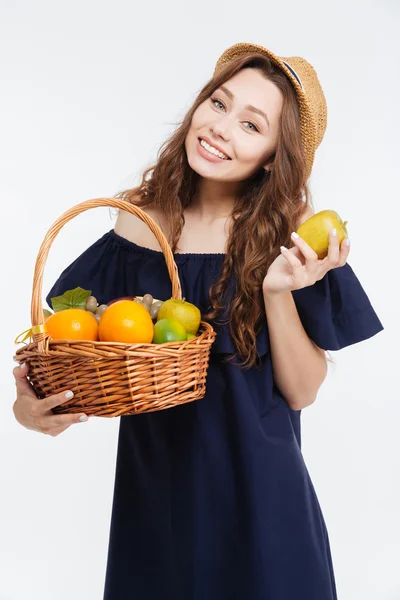 Χαρούμενα χαριτωμένο νεαρή γυναίκα με το καπέλο κρατά το καλάθι με φρούτα — Φωτογραφία Αρχείου
