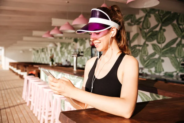 Mujer deportiva escucha música con auriculares y smartphone en la cafetería — Foto de Stock