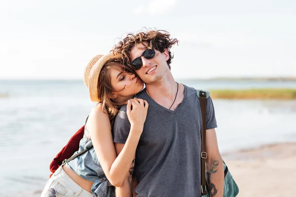 Pareja con mochilas de pie y besándose en la playa —  Fotos de Stock