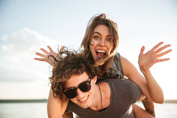 Jeune couple souriant heureux en amour piggyback à la plage — Photo