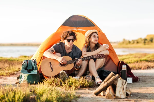 Retrato de una joven pareja sentada con la guitarra cerca de la hoguera —  Fotos de Stock