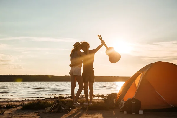 Vista posteriore di coppia che tiene la chitarra e abbraccia al tramonto — Foto Stock